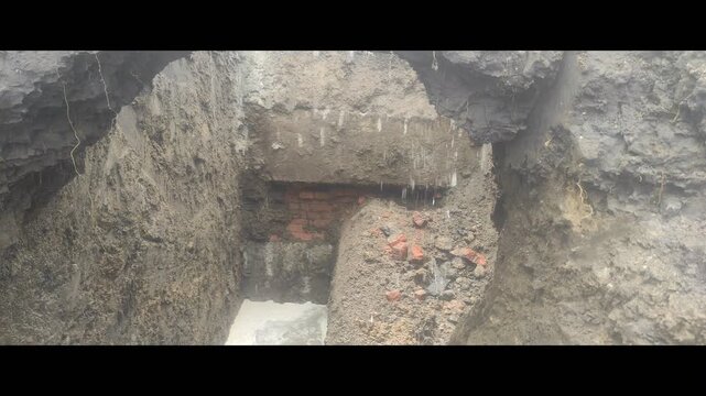 Close up of a deep construction pit with old brick foundation and leaking water at a repair site