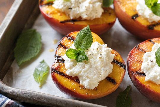 Grilled peach halves topped with creamy ricotta cheese and fresh mint leaves served on a rustic baking sheet for a healthy summer dessert or gourmet appetizer.