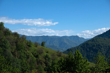 Obraz premium Scenic landscape of green mountain ridges and valleys under blue sky with clouds