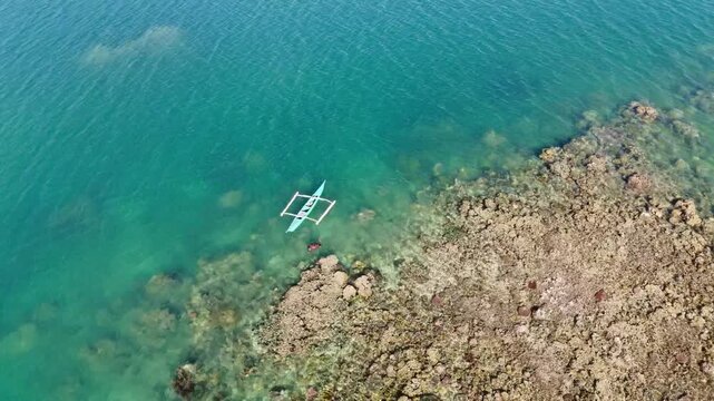 Aerial view of person snorkeling near outrigger canoe on tropical coral reef vibrant turquoise ocean.