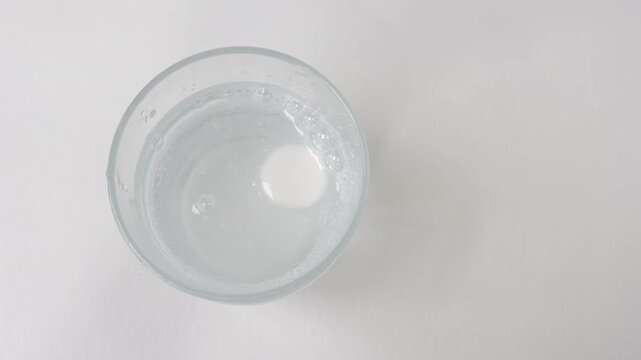 Top view of an effervescent tablet dissolving in a glass of water, releasing bubbles and fizzing on a white background, representing medicine, vitamins, or a hangover cure