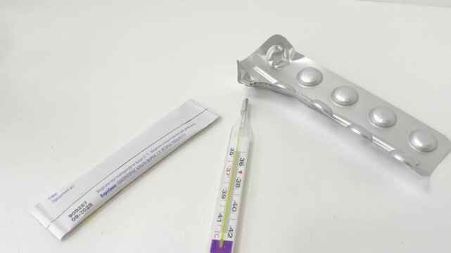 Mercury thermometer with pills in a blister pack and powdered medicine sachet on a white background, representing fever treatment and healthcare during illness