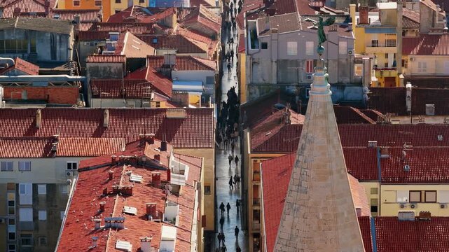 Aerial view of narrow street in Zadar old town with people walking between historic red tiled roofs.