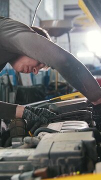 Mechanic in car repairing service - diagnostics in engine compartment