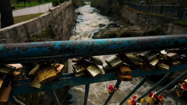 Many colorful love locks attached to a blue metal bridge railing with peeling paint. Fast-flowing river visible in the background, creating a romantic contrast with nature.
