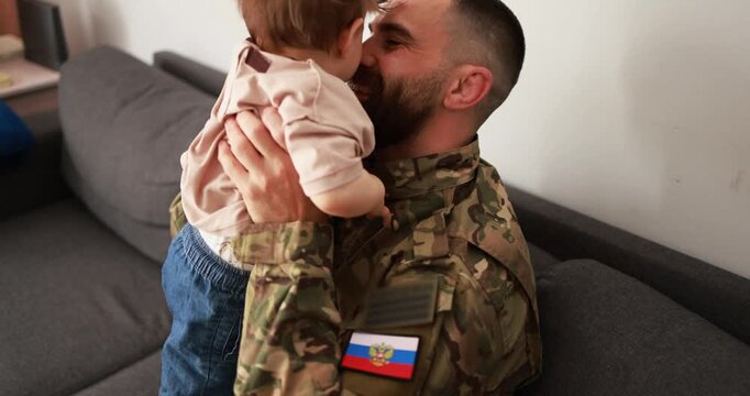 Male russian soldier in military uniform hugs his little son at home - Emotional military happy homecoming concept 
