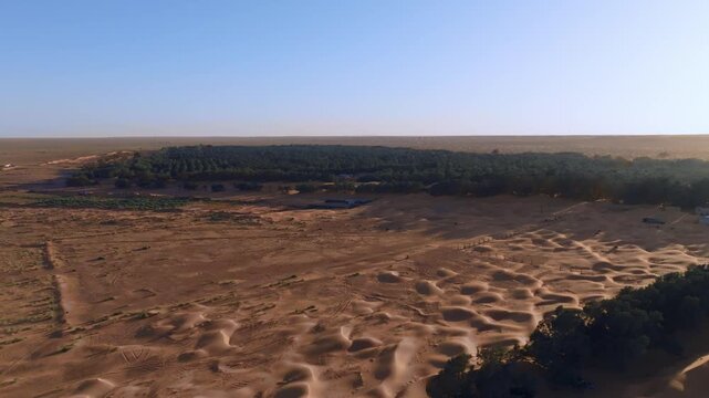 Aerial drone flight over the remote Ksar Ghilane Oasis in the heart of the Tunisian Sahara. Panoramic view of the desert outpost surrounded by endless sand dunes and vast arid wilderness