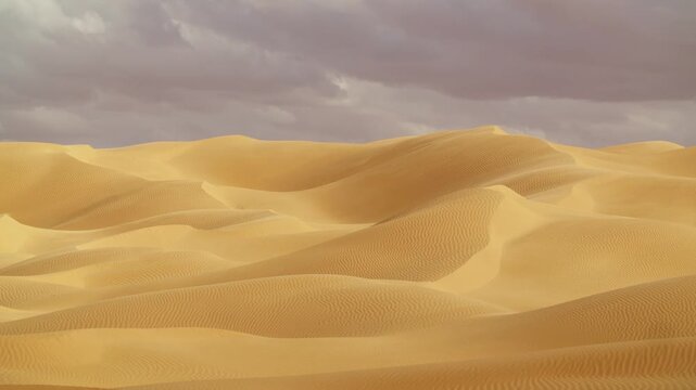 Aerial view of the Sahara Desert in Tunisia, capturing the rhythmic patterns of sand dunes as strong winds create a light haze of blowing dust over the arid landscape