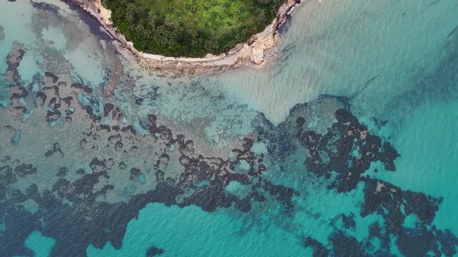 Aerial top down tracking shot of a rocky coastline and crystal clear turquoise sea water with underwater reef patterns in North Corfu, Greece