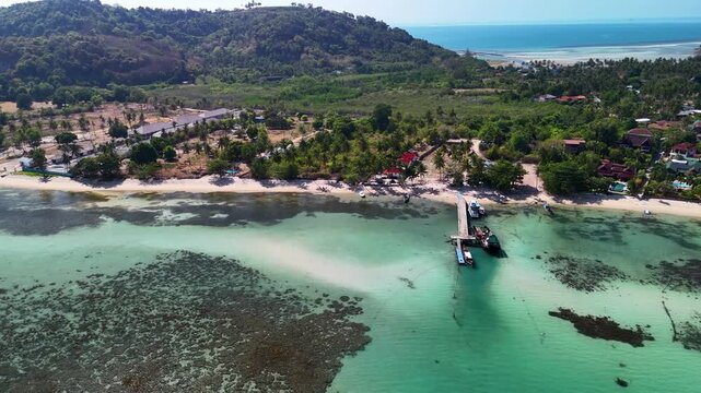 Aerial drone view of Koh Rong Island featuring tropical beach, turquoise shallow water, coral reef patches and wooden pier along Cambodia coastline
