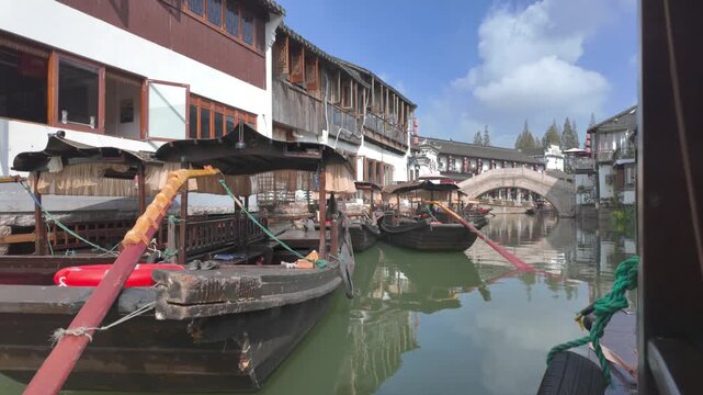4K video of Zhujiajiao ancient water town filmed from a boat passing old gondola style boats parked near historical buildings in China