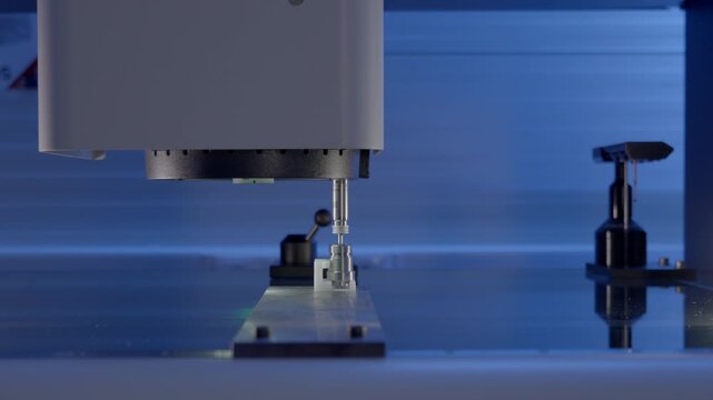Optical metrology machine analyzing dimensions of a precision CNC manufactured part with illuminated inspection lighting.