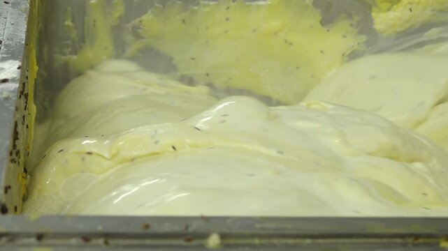 Thick yellow cheese mixture being processed in an industrial cheese factory machine, showing smooth dairy texture during production.