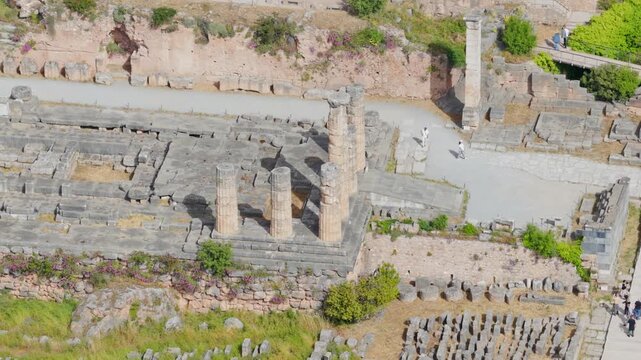 Majestic view of the temple of Apollo, an ancient greek archaeological site in Delphi, Greece, with tourists walking along the paths admiring the historical doric columns and stonework
