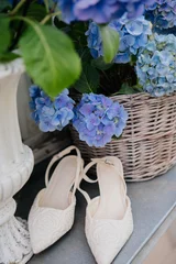 Fototapeten Hortensie A pair of chic white slingback bridal shoes with textured embroidery patterns placed near a rustic wicker basket filled with blooming blue hydrangea flowers.   © Oleksandra Dyka