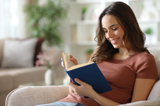 Happy woman reading a paper book sitting on armchair