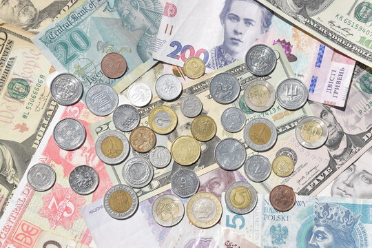 Close-up top view of scattered money: Ukrainian 200 hryvnia, US 20 dollar bills, and Polish zloty banknotes with a variety of silver and gold-toned coins.
