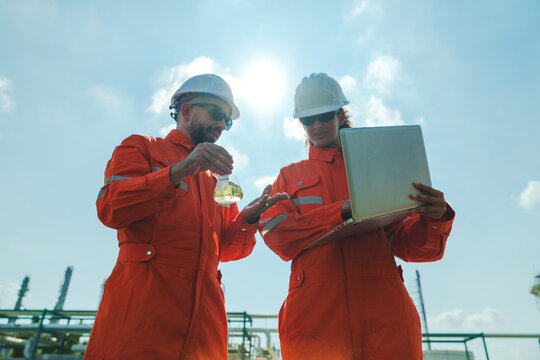 Oil and gas refinery in petroleum industry with inspection engineer, industrial engineer safety helmet orange coverall laptop outdoor inspection worker team sky laboratory