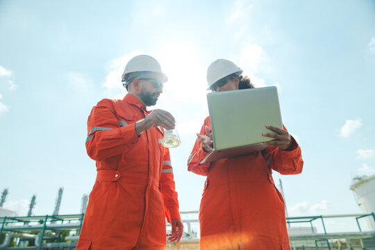 Oil and gas refinery in petroleum industry with inspection engineer, industrial worker safety helmet orange coverall laptop laboratory refinery engineer outdoor teamwork inspection plant hardhat