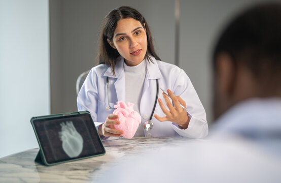Female cardiologist doctor explaining coronary artery disease, heart failure and valve problem to patient, physician using tablet and model for diagnosis, cardiology, surgery and insurance concept