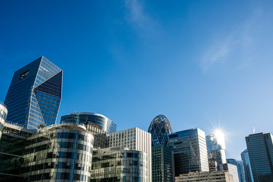 Sun flare glints across the La Defense Paris France skyline, where glass skyscraper architecture rises over an urban business district
