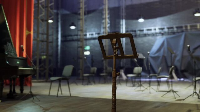 Empty industrial studio stage with piano, metal truss and exposed rigging, scattered chairs and music stands, warm practical lighting and gritty textures, band