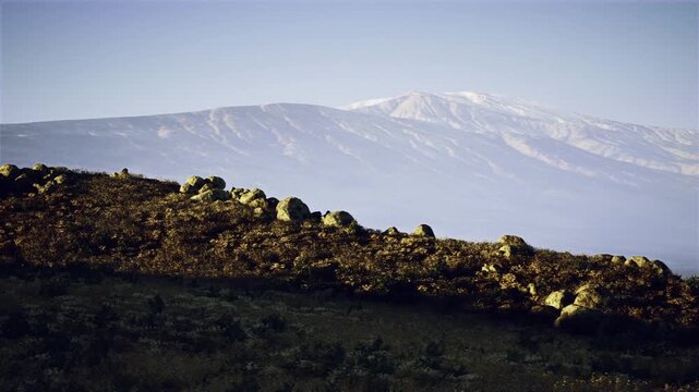 Silhouetted ridge in foreground with snowcapped peak behind, dramatic expedition staging scene, strong contrast, rugged foreground texture and crisp alpine
