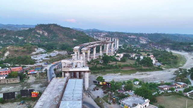 Drone flight over unpaved concrete flyover deck and rebar. High-angle aerial drone footage tracking along the curved, unpaved deck of a massive highway bridge construction project. 