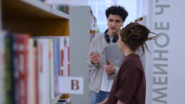 Smooth Tracking Movement Following Curly-Haired Guy and Dreadlocked Girl as They Laugh and Walk Past Book Rows