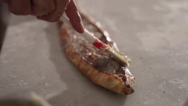Professional chef brushing melted butter on freshly baked Turkish pide on a red cutting board, fa01