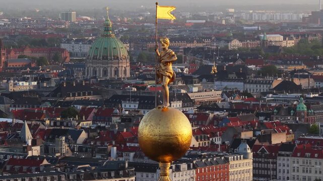 Aerial view of golden statue on church of our saviour spire with Copenhagen cityscape and Frederiks church in background.