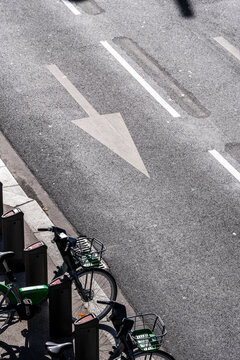 A white arrow on asphalt guides a bicycle lane along a quiet Lyon street, where shadow, parking, mobility and direction meet at the curb.