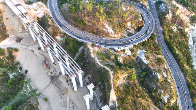 Top-down aerial drone footage capturing transport trucks and commuter vehicles navigating a sweeping S-curve on a major national highway. 