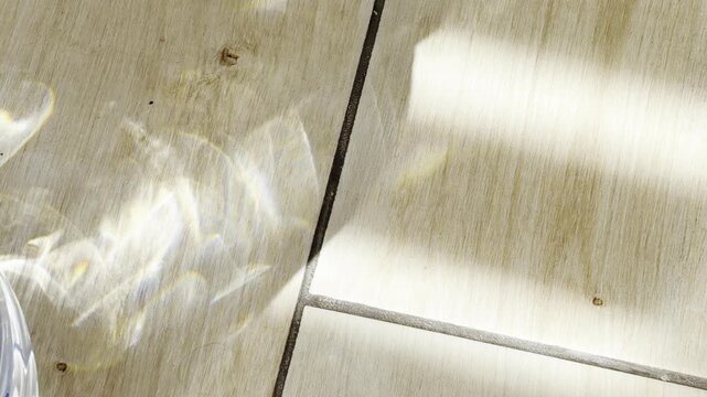 Morning light and caustic reflections from a water glass dancing on a sunlit wooden floor, creating mesmerizing patterns and an abstract, bright, and airy atmosphere
