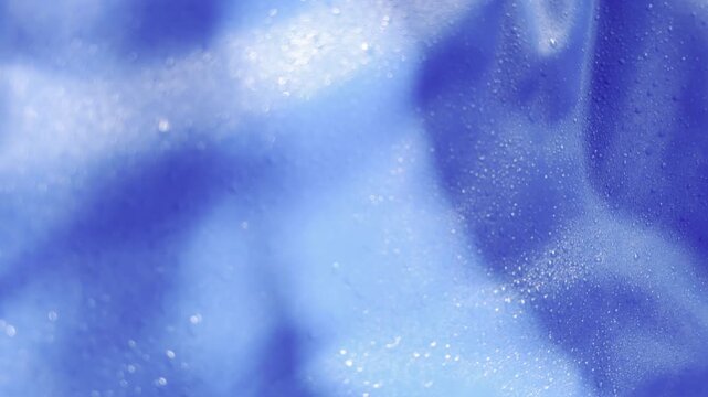 Macro view of tiny water drops condensing and shimmering on a crumpled blue plastic surface, with soft light creating a mysterious and abstract slow motion visual effect