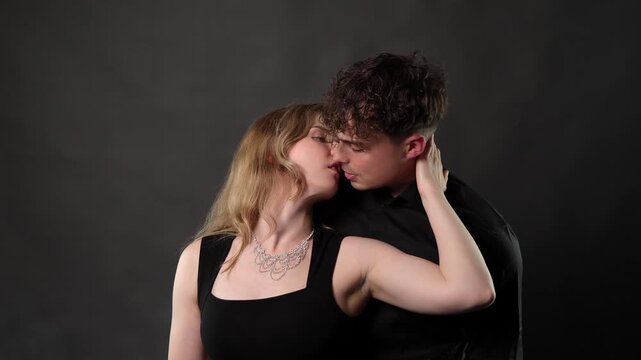 Love and affection, a young romantic couple is shown kissing and embracing intimately against a dark background. This footage can be used in commercials, documentaries, or editorial content to convey 
