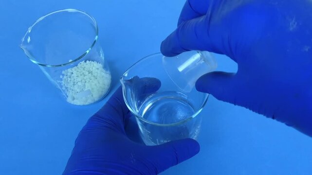 Gloved hands preparing an emulsion in a beaker by mixing two different liquid phases