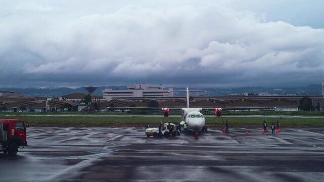 Small propeller plane parked on wet airport tarmac with ground crew members working nearby
