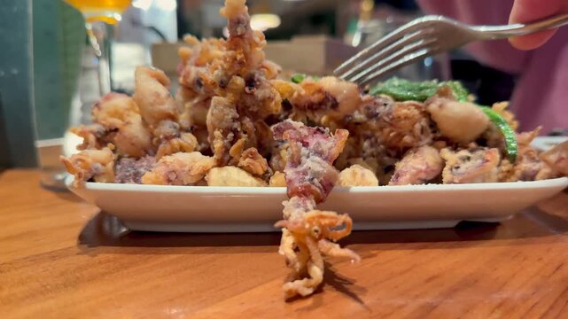 Closeup view of the hand of a caucasian man eating andalusian style fried calamari with a fork in a traditional bar.