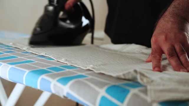Man ironing white shirt on patterned board completing a common household chore