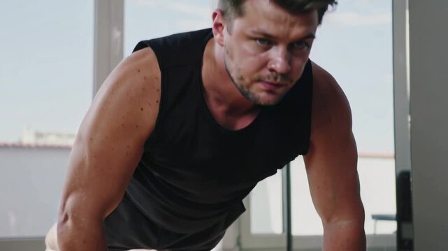 Starting low-angle camera, man doing pushups on hardwood floor training in black tanktop and shorts