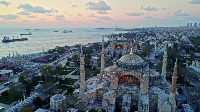 Breathtaking aerial drone video over Istanbul's historic Sultanahmet at twilight. Hagia Sophia & Blue Mosque glow, Bosphorus, cargo ship. Timeless Turkish landmark panorama.
