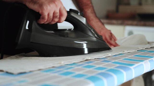 Man ironing wrinkled clothing on a blue and gray patterned board in a home