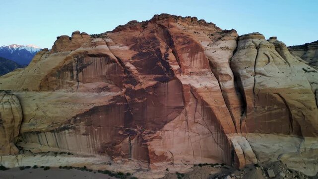 Drifting drone camera revealing sandstone cliff face at desert plateau, with dark varnish stain