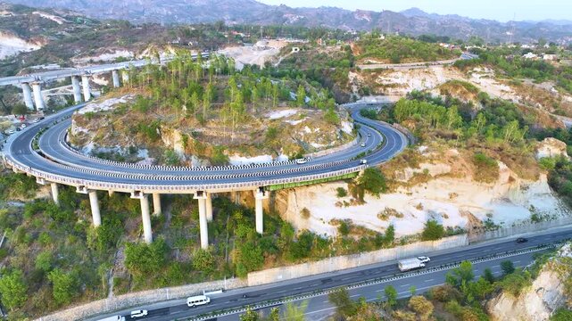 Drone sweeping shot of vehicles on newly developed curved highway. Dynamic drone tracking shot following a line of cars and trucks traversing a beautifully engineered S-curve road. 