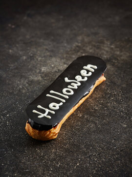 The image shows a Halloween-themed eclair topped with a dark chocolate glaze and decorated with white writing. This dessert is ideal for seasonal promotions, holiday menus, and festive events
