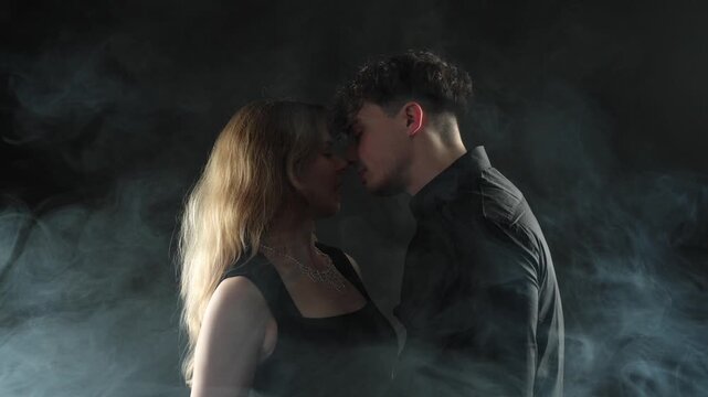 Passionate love and romance, a young couple is shown kissing intimately in a smoky, dark studio setting in cinematic slow motion. This footage is projects related to relationships, emotional connectio