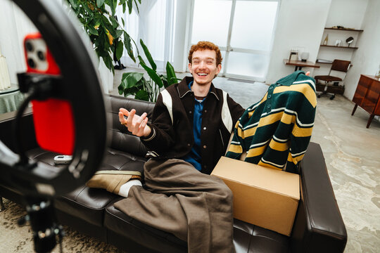 A clothing-focused fashion creator presents products with a smartphone in a home studio.