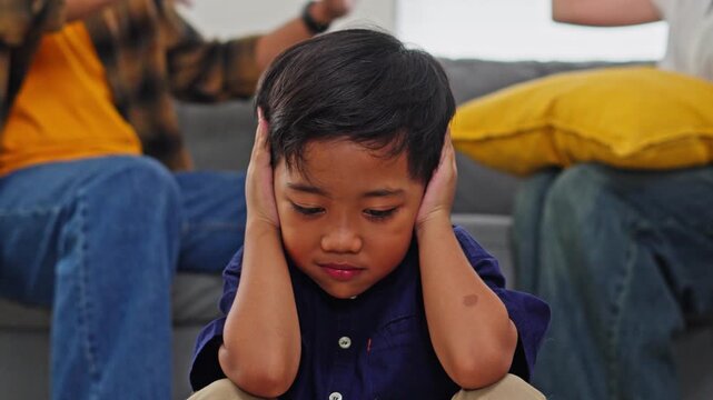 Stressed child blocking out noise while parents have heated discussion behind him