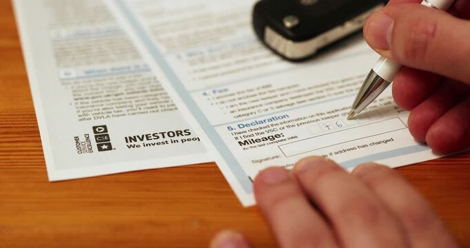 A person completes a vehicle mileage declaration form for a registration certificate type V62 using his pen.